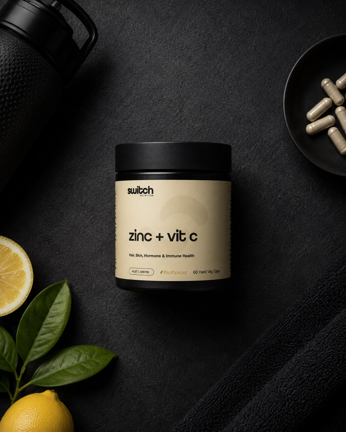 Supplement container labeled 'zinc + vit c' by 'switch' on a dark surface with lemons and leaves.