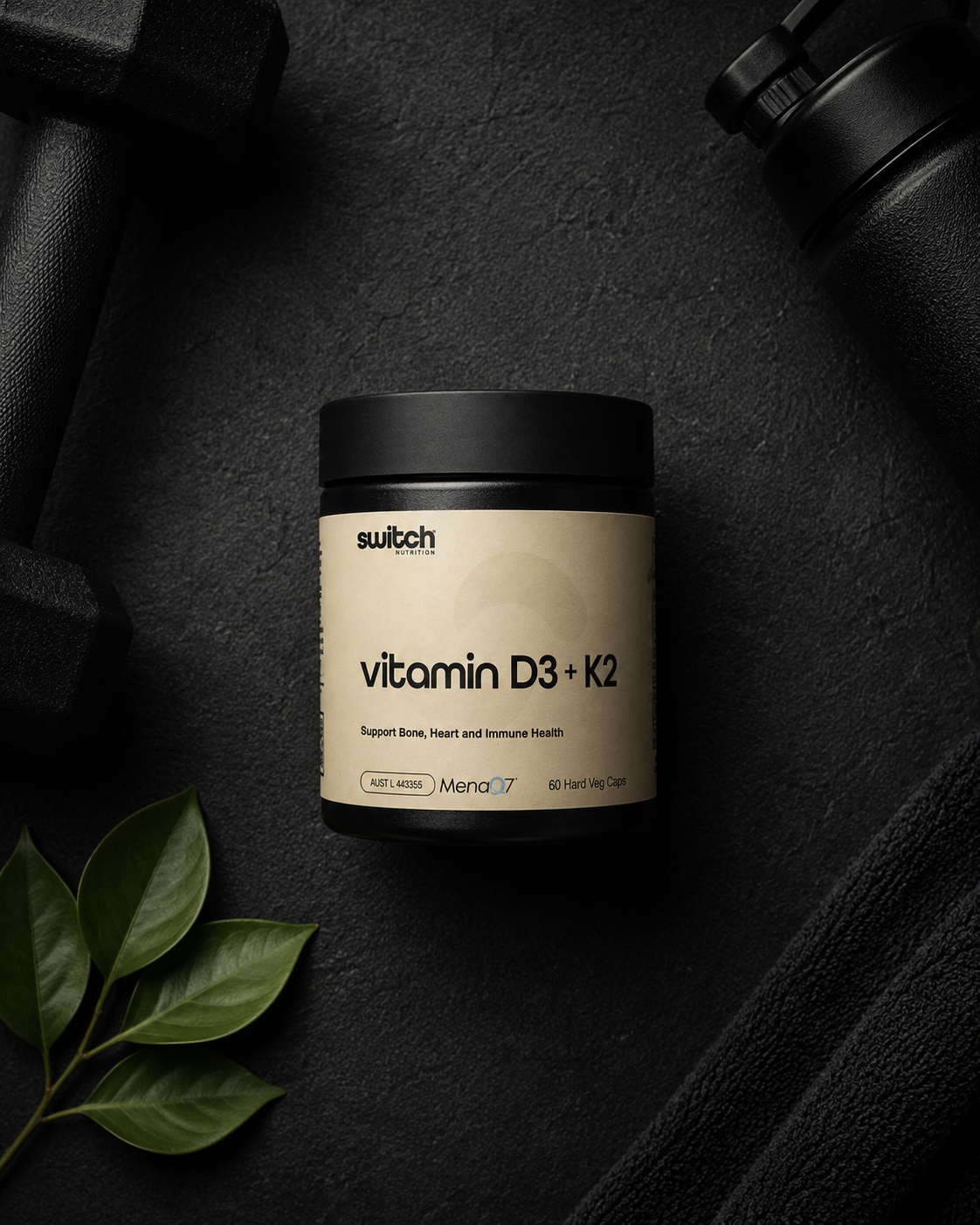 Container of switch vitamin D3 + K2 on a dark surface with green leaves.