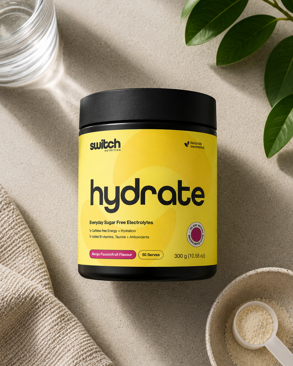 A jar of Switch Hydrate sugar-free electrolytes powder, shown in a styled flat-lay setting with a glass of water, a beige towel, and a small bowl of powder.