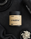 Container of switch creatine on a black surface with additional creatine capsules.