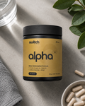 A black supplement jar labeled 'switch alpha' with a mustard-yellow label, styled on a light gray surface with capsules in a bowl, a glass, and green leaves around it.