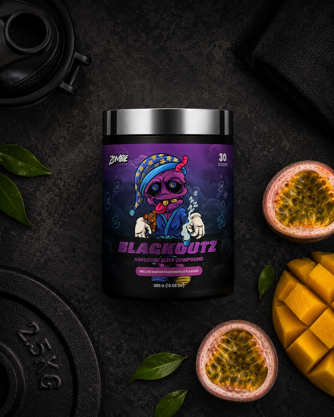 A tub of Blackoutz Sleep Compound powder, featuring a purple label with a cartoon character, styled in a flat lay with mangoes, passion fruit, and gym weights on a dark textured background.