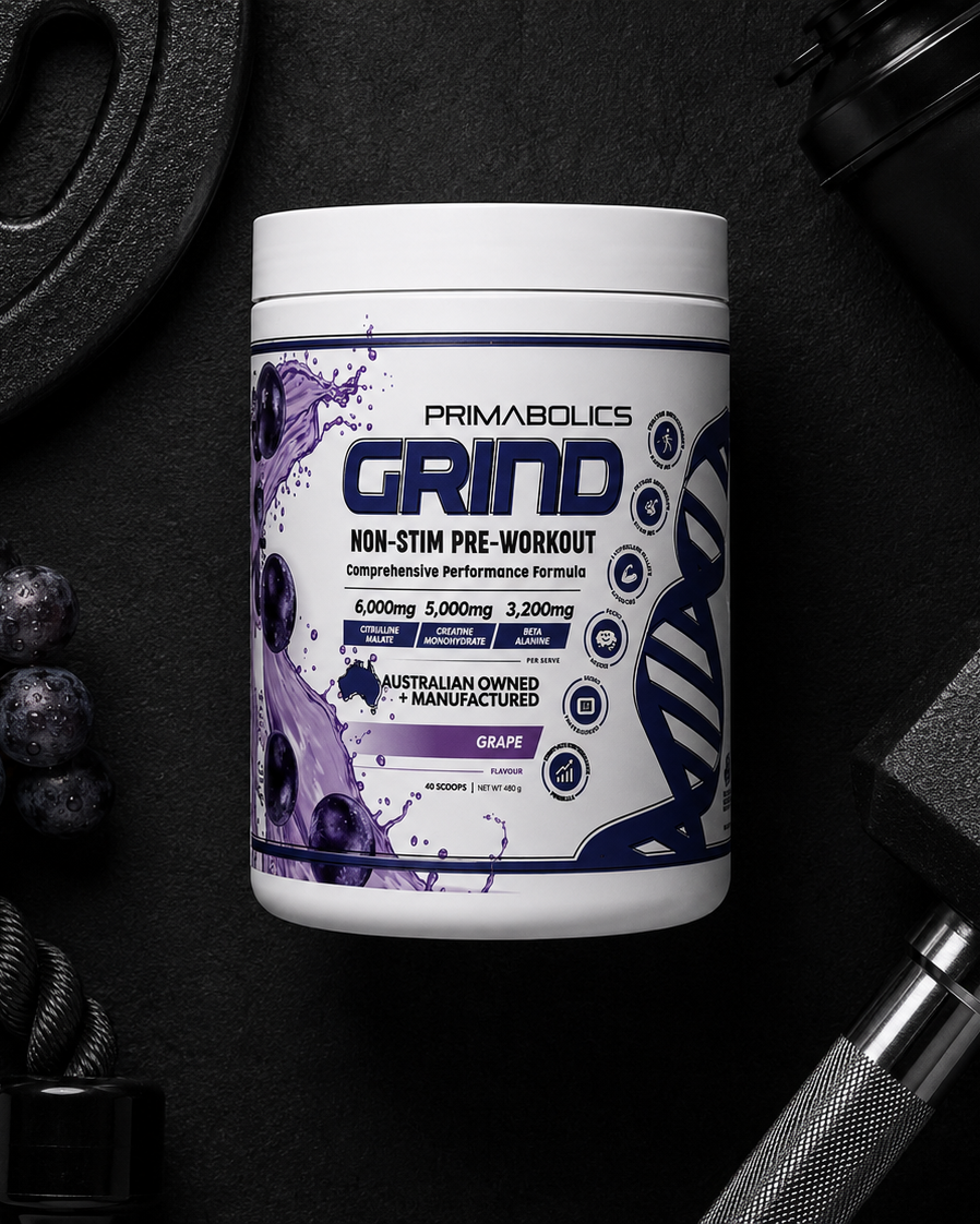 Primabolics Grind pre-workout supplement container on a dark surface with gym equipment.