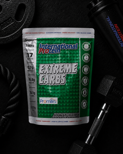 International Protein Extreme Carbs supplement package on a dark background with gym equipment.